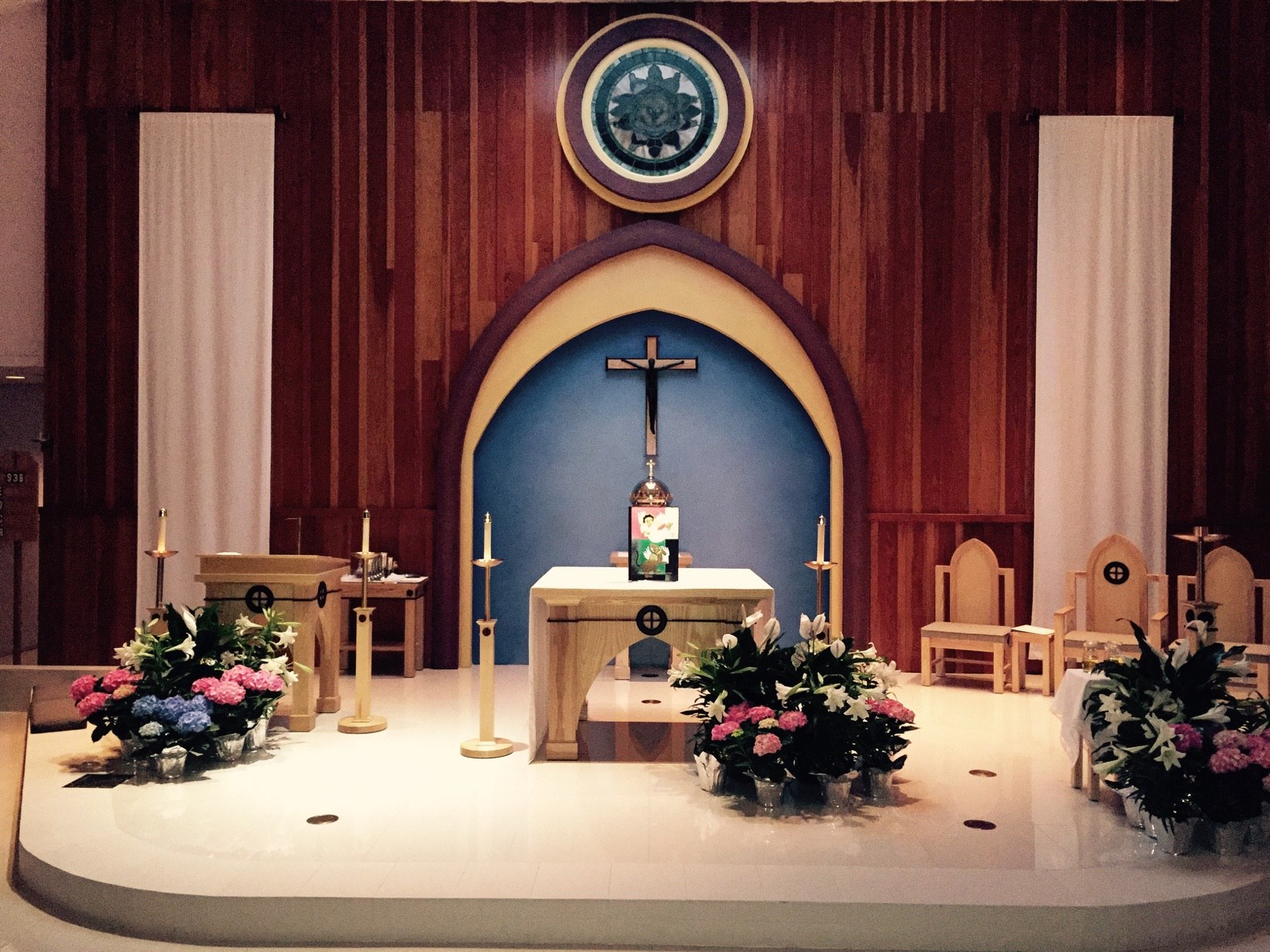 The sanctuary of Holy Redeemer Catholic Church: a wooden altar beneath a crucifix set in a blue arch, framed by candles and Easter flowers
